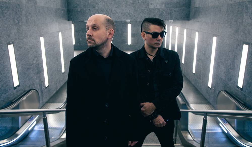 Fixed Lens band members standing in front of escalators with lights and surveillance cameras behind them
